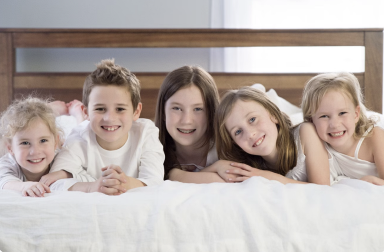 Children sitting on My Green Mattress bed smiling at camera