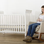 Expecting mother sitting beside Emily organic crib mattress in nursery