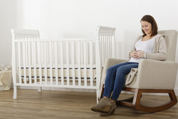 Expecting mother sitting beside Emily organic crib mattress in nursery