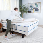 Man putting organic topper on mattress in bright natural bedroom setting