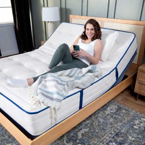 A woman sitting comfortably on the Natural Escape Organic Mattress that is on an adjustable base.