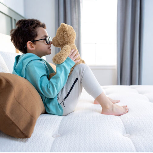 A child playing with a teddy bear on the Pure Eco Organic Kids Mattress, highlighting the mattress’s 365-night sleep trial and 20-year warranty.
