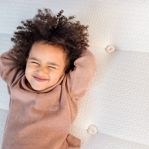 A child smiling while lying on the Pure Eco Organic Kids Mattress, showcasing its hand button tufting that adds durability and comfort.