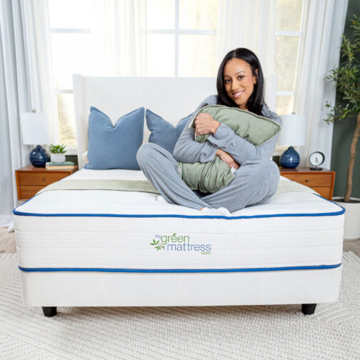 A woman sitting on the Kiwi Organic Mattress, highlighting the Madison spring system and zoned support that provides edge support and contouring comfort.