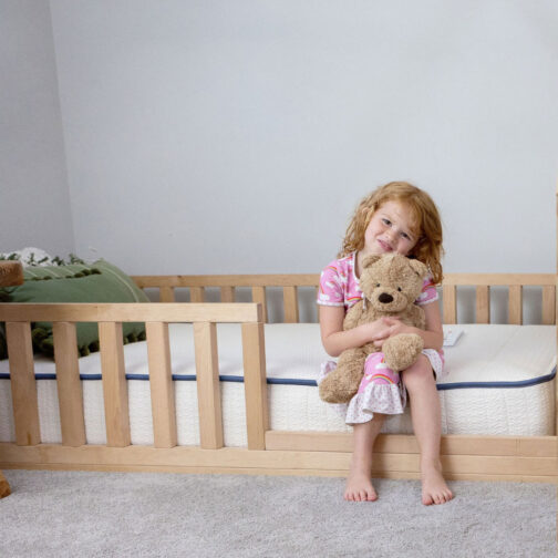 A young child sitting on the Pure Eco Organic Kids Mattress in a low-profile floor bed frame, highlighting its 8-inch height ideal for bunk beds, floor beds, and trundle beds.