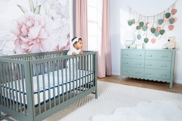 Baby standing in crib on the Emily Organic Crib Mattress by My Green Mattress in a floral nursery.