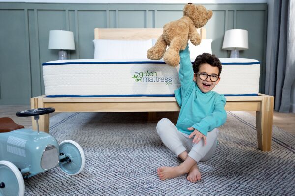 Smiling child sitting on the floor next to the Pure Eco Organic Kids Mattress by My Green Mattress.