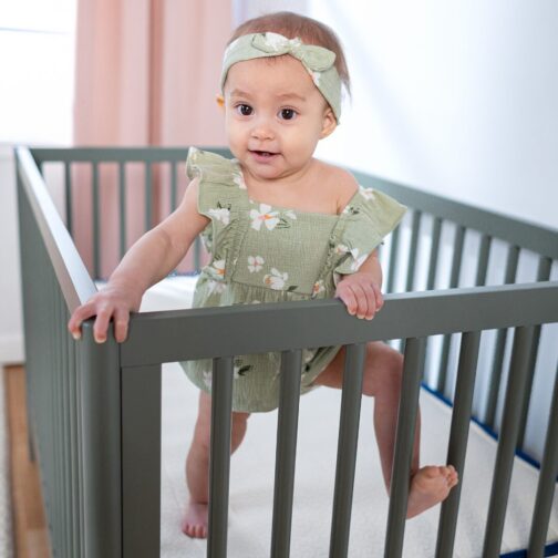 Baby standing on the Emily Organic Crib Mattress, highlighting the 10-year warranty and 365-night sleep trial.