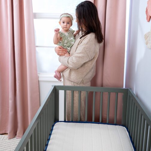 Mother holding baby next to the Emily Organic Crib Mattress, which features GOLS-certified organic coconut coir for natural firmness.