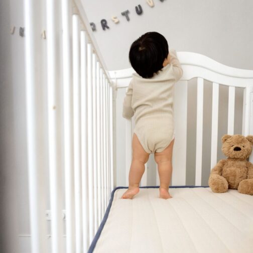Baby standing on the Emily Organic Crib Mattress with breathable GOTS organic cotton and natural wool the chemical-free flame retardant.